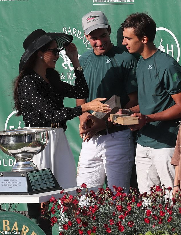 Body language expert Judi James said: 'Meghan attempts to take the wooden box, likely Champagne, from the hands of the other player, but he refuses to let go'