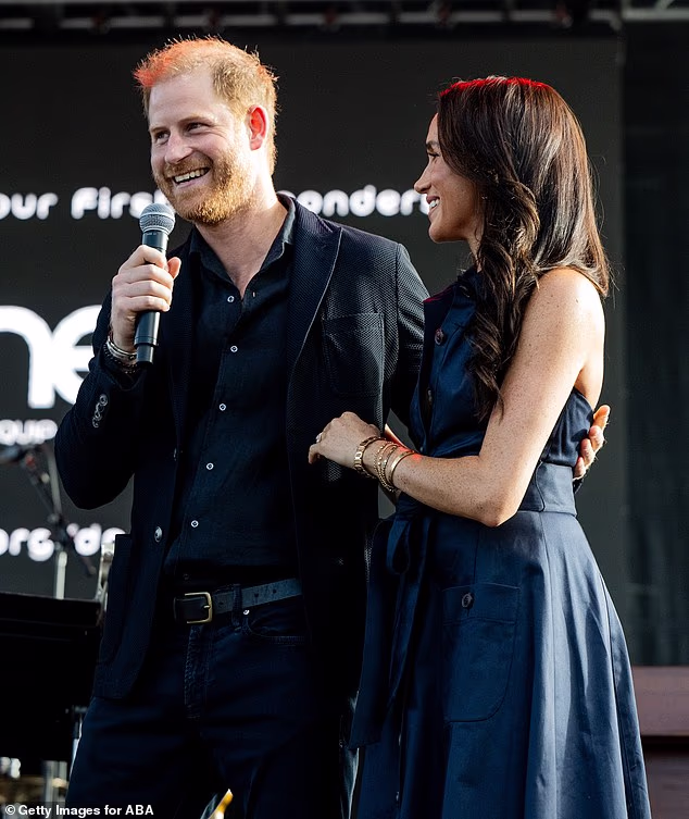 Meghan cut a sophisticated figure in a midnight blue Caroline Herrera collared halterneck dress with tortoiseshell buttons and a waist-cinching sash for the outing on Saturday