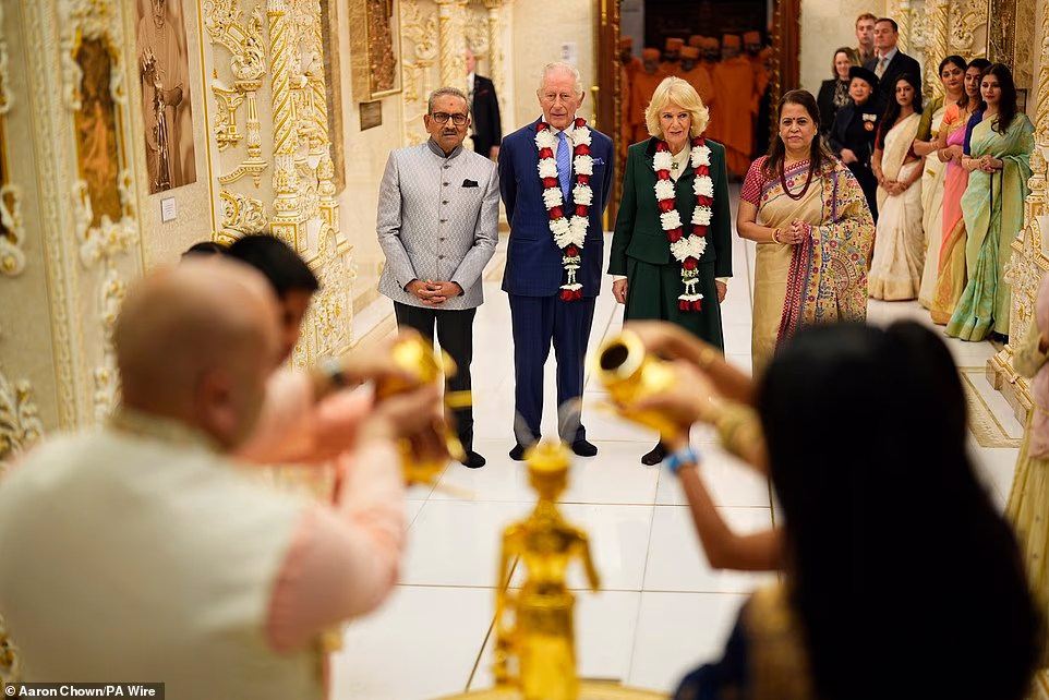 There the King observed a young boy offering petals to the central shrine for Bhagwan Swaminarayan, the principal deity of the temple, before the Queen observed a young girl do the same. Mr Patel explained the details of the pillars and shrines to the King who nodded and appeared engaged. Downstairs, the King and Queen observed a family of four perform an Abhishek—a ceremonial pouring of water over a deity's image. The King asked the family how often they performed an Abhishek and whether the children were off school for half term. The family told him about the festivities and fireworks for Diwali just over a week before. Leaving the Abhishek, the King said to them, 'Well, very happy belated Diwali.' In the Haveli foyer, the royals then met trustees of BAPS before viewing a model of the BAPS Mandir in Paris. They spoke to the Commissioner of India to the UK, the Ambassador of France to the UK and architects and craftsmen involved in the project, one of whom showed the King a wooden piece of carving from the ceiling.