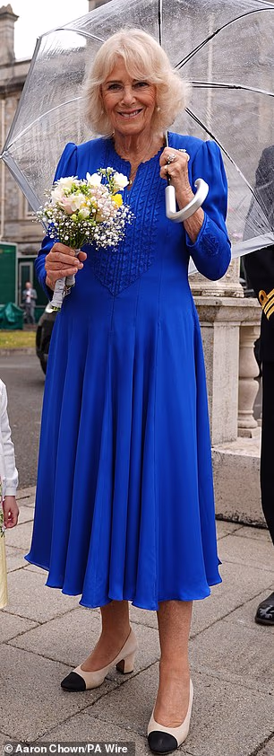 During a visit to HMNB Devonport in Plymouth, Camilla wore a striking cobalt blue Fiona Clare dress featuring softly puffed shoulders, embroidered bib detailing and a signature front zip