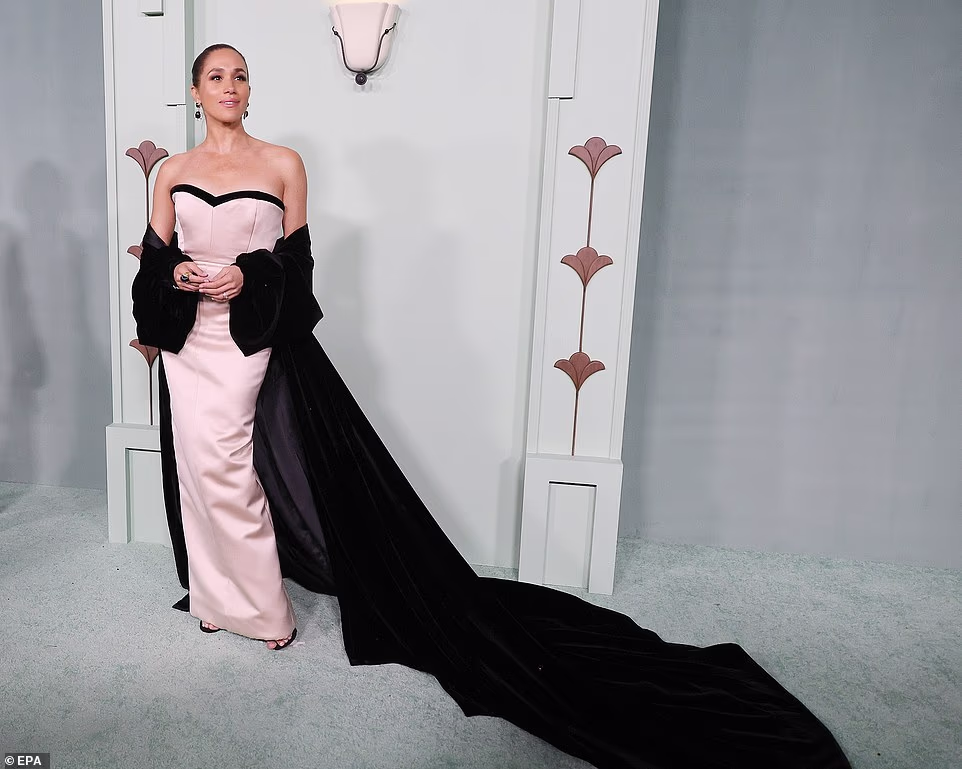 Meghan Markle went solo, donning a pink strapless dress with an enormous velvet black train at the annual Fifteen Percent Pledge Fundraising Gala last night. The Duchess of Sussex posed on the red carpet in Los Angeles co-ordinating the billowing sleeves of the train with her earrings, shoes and sweetheart neckline. Dripping in jewellery she appeared relaxed at the gala honouring Beyonce's mother Ms Tina Knowles for her leadership, advocacy, and commitment to empowering Black communities and creators. She confidently posed, flaunting her figure and grinning in the baby pink tailored number. Her custom gown was designed by Charles Harbison of Harbison Studio, a New York-based luxury womenswear brand.