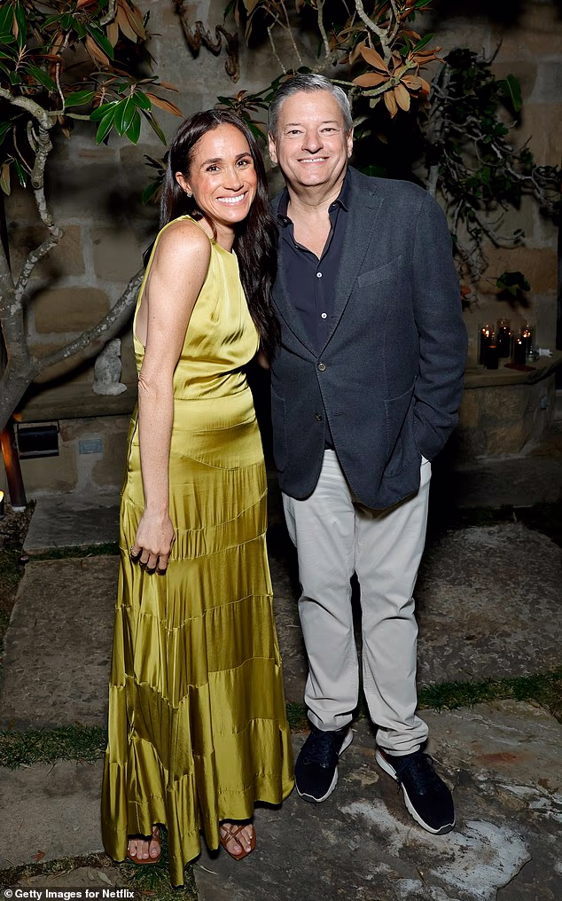 Meghan, wearing an olive green dress and sandals, smiles for a photo with Netflix boss Ted Sarandos