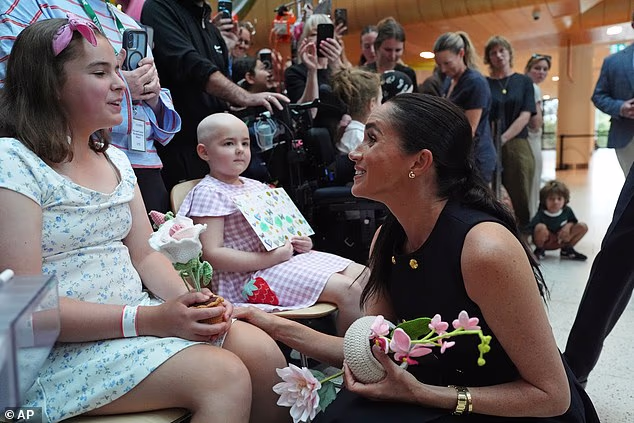 The Duchess knelt as she was handed flowers by a young patient