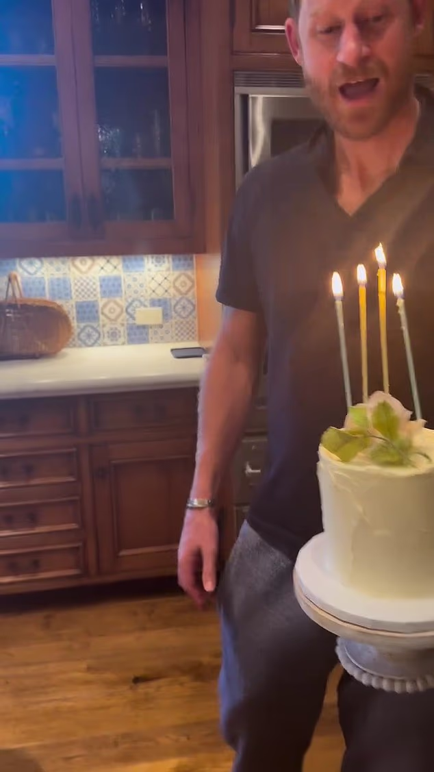 The Duke of Sussex, dressed in grey tracksuit bottoms and a blue polo shirt, helps blow out the candles, before Meghan affectionately tells him 'I love you'.