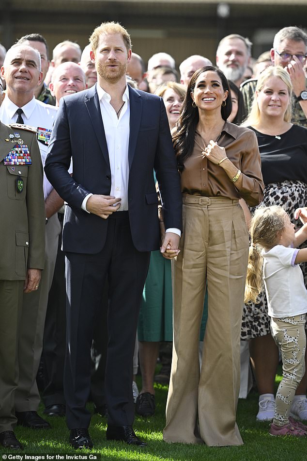 The royal couple hold hands as they pose for pictures. Meghan wore loose fitting wide leg caramel trousers and a silky brown shirt. Harry wore a blue suit but no tie