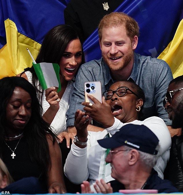 The couple laughed, while Meghan waved a Nigerian flag, as they took selfies with others within the crowd