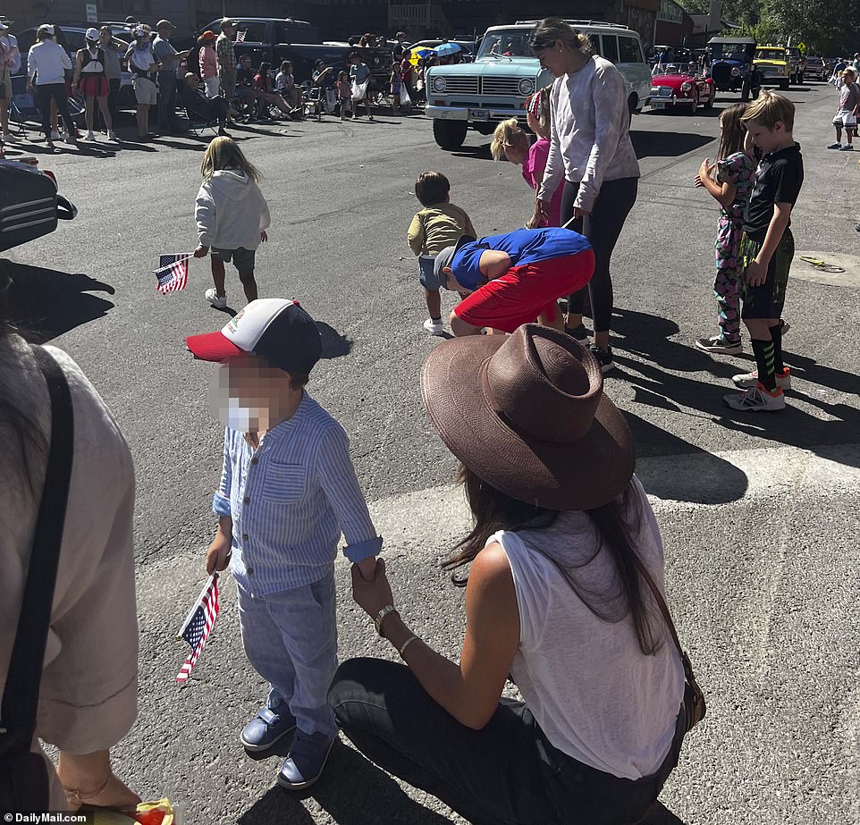 Images obtained exclusively by DailyMail.com reveal the young family sitting down on a dusty sidewalk as they watch a procession of floats, tractors and cowboys and rodeo girls on horseback.