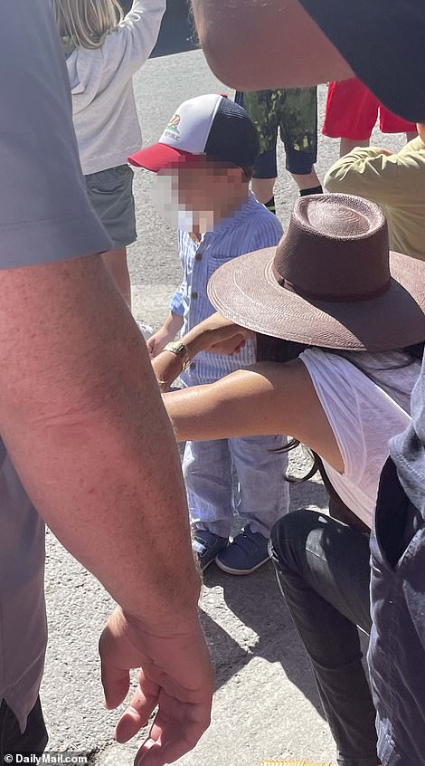 The parents were seen doting on their son, who can be seen sucking on a red lollipop and holding a mini American flag on the dusty sidewalk of the town's thoroughfare