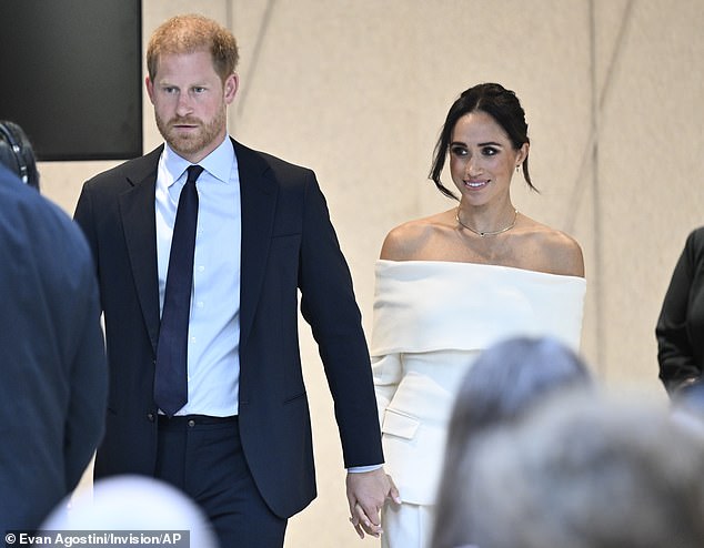 Meghan looked elegant in her white strapless blazer, which she paired with a simple necklace, while her brunette locks were swept into an updo