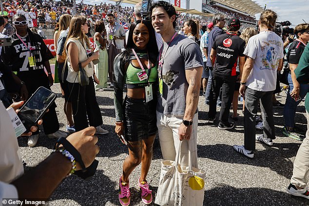 Joe Jonas poses for a photo with a fan, while carrying a white tote bag and rocked white pants for the race day excursion