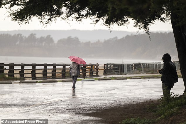 People walk through wet conditions along Seacliff State Beach in Aptos, California on Wednesday, Dec. 20, 2023