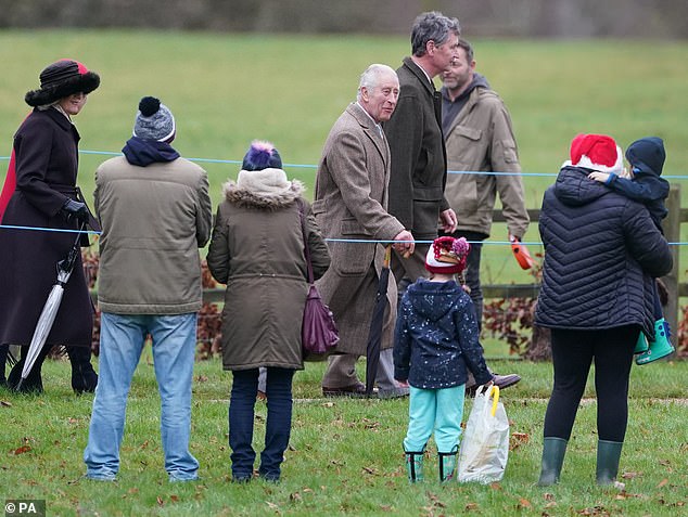 Queen Camilla, dressed in a warm wool coat and black feathered hat strolled behind the King, smiling at families gathered