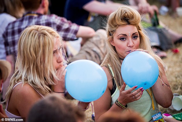 Neurologists have warned that nitrous oxide, a gas inhaled recreationally by some young people, is more dangerous than cocaine. Pictured: Revellers suck on balloons at a music festival, a common way people inhale nitrous oxide