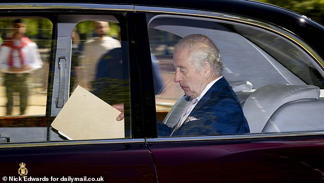 King Charles III is pictured holding papers as he arrives at Clarence House in London today