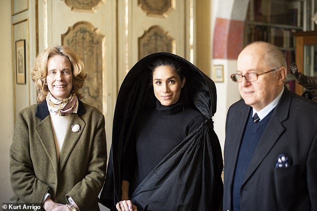 Meghan tries on a traditional Maltese cloak, called a ghonnella, which belongs to the 9th Marquis de Piro (right) and his wife Frances (left)