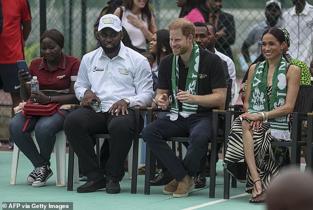 Harry is seen giving a slight smirk, while sitting next to Meghan who appears to have a huge grin on her face