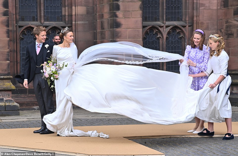 A bridesmaid and the mother of the bride struggle to keep Olivia's veil down in the wind