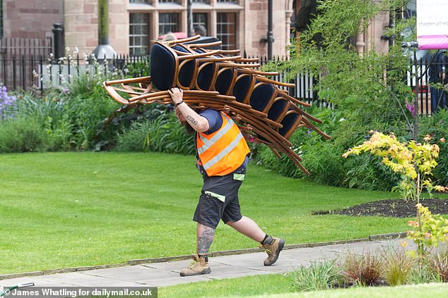 A workman carries a bundle of chairs through the garden at Chester Cathedral