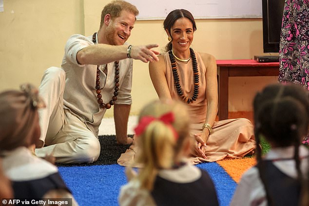 Harry and Meghan smile as they meet children at the Wuse Lightway Academy in Abuja today