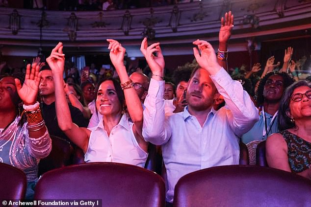 Meghan and Harry lift their hands up as they attend the Afro Women and Power event