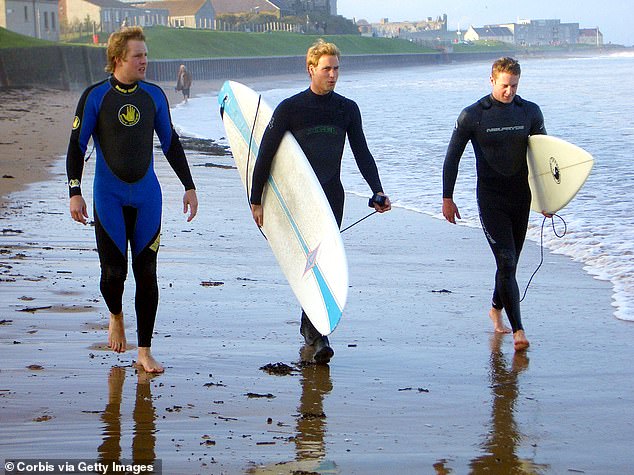 Prince William carrying a surfboard with his friends along the shore in Scotland in 2004