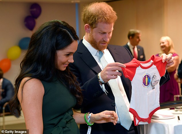 Meghan and Harry look at a baby grow gifted to them for Archie at the awards in 2019