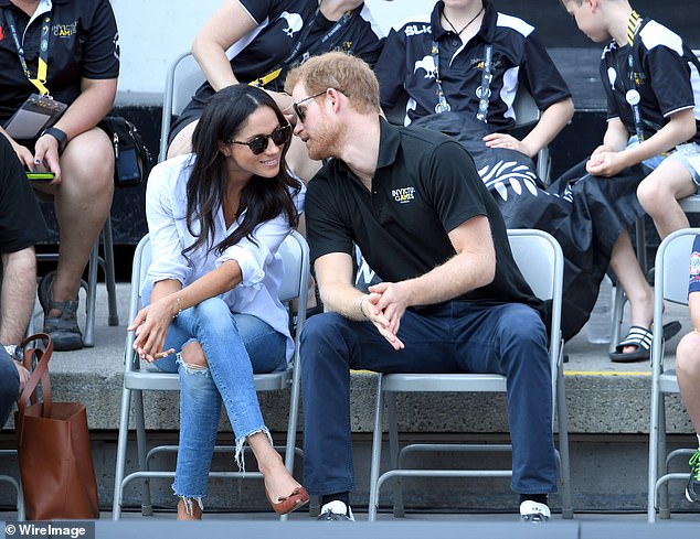 The Prince leaning in to chat to Meghan, who is wearing The Husband shirt by Misha Nonoo