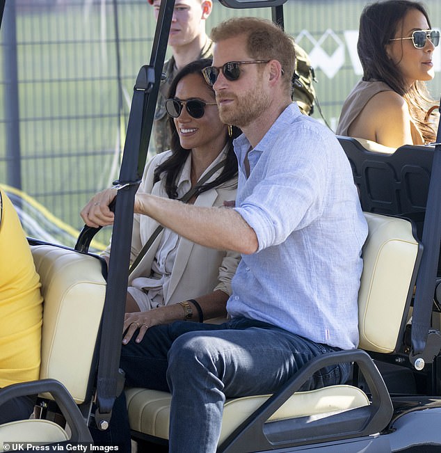 The Duchess smiles as she holds Harry's leg while they attend a cycling event for the Invictus Games in Germany last year