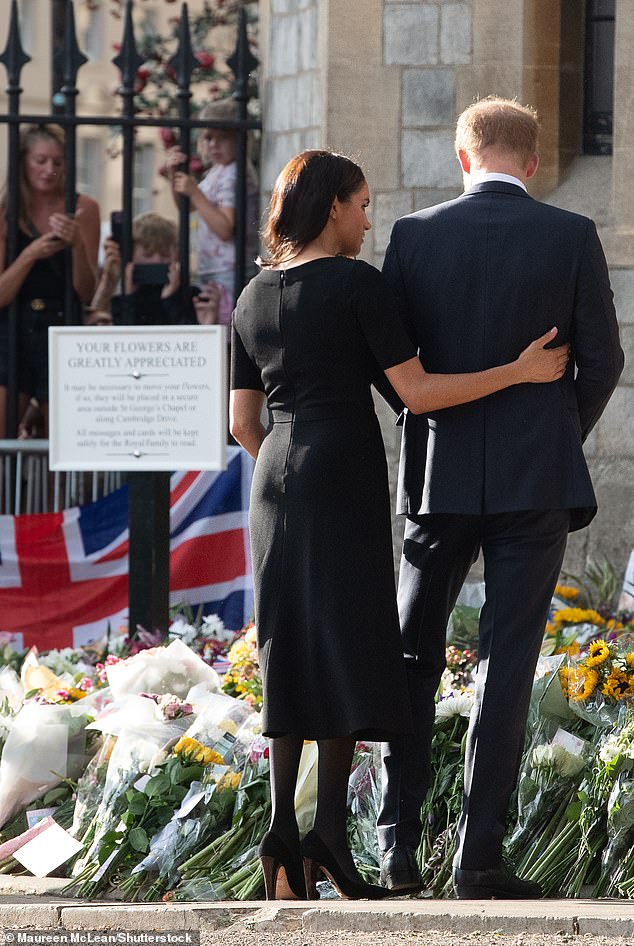 The Duchess wraps her arm around Harry's back as they look at flowers left in tribute to the late Queen Elizabeth on September 10, 2022