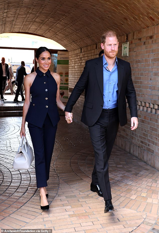 Harry's hand is placed on top of Meghan's and his arm in front as they walk in Bogota, Colombia