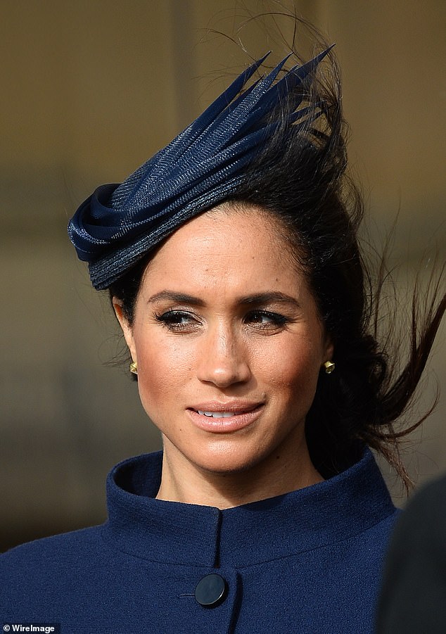 Meghan wearing a navy coat and matching head piece to Eugenie's wedding in 2018