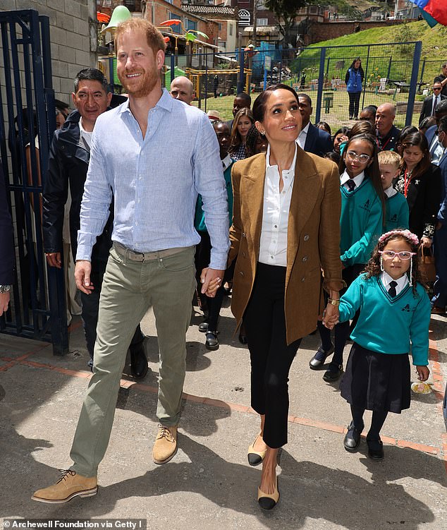 Harry and Meghan are photographed holding hands as they walked into Colegio La Giralda in Bogota, Colombia, in August