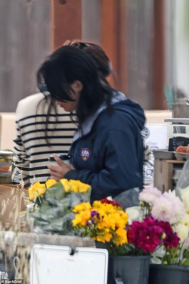 Meghan (pictured in the background in a striped top)  was spotted picking up supplies at a farmer's marker in Montecito before heading into a car and driving off in June amid rumours she was shopping for her show