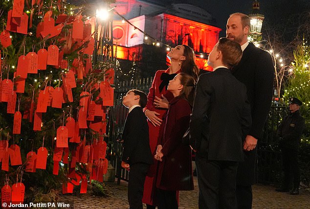 The Prince and Princess of Wales with their children Prince George, Princess Charlotte and Prince Louis look at messages on the Kindness Tree ahead of the Together At Christmas carol service