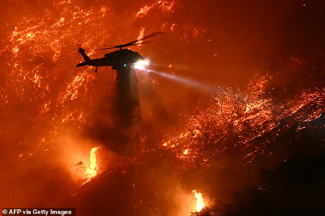 A fire fighting helicopter drops water as the Palisades fire grows near the Mandeville Canyon neighborhood and Encino, California, on January 11, 2025