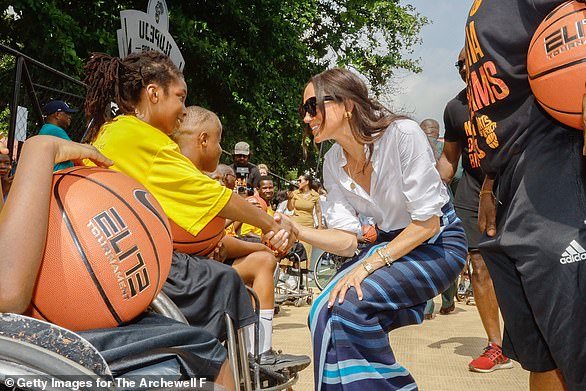 Meghan in traditional Nigerian blue wrap skirt to watch the basket ball