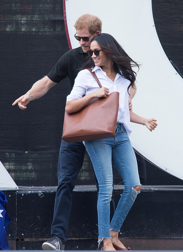 Harry guiding Meghan during their first official appearance together, she is wearing ripped denim jeans and sunglasses