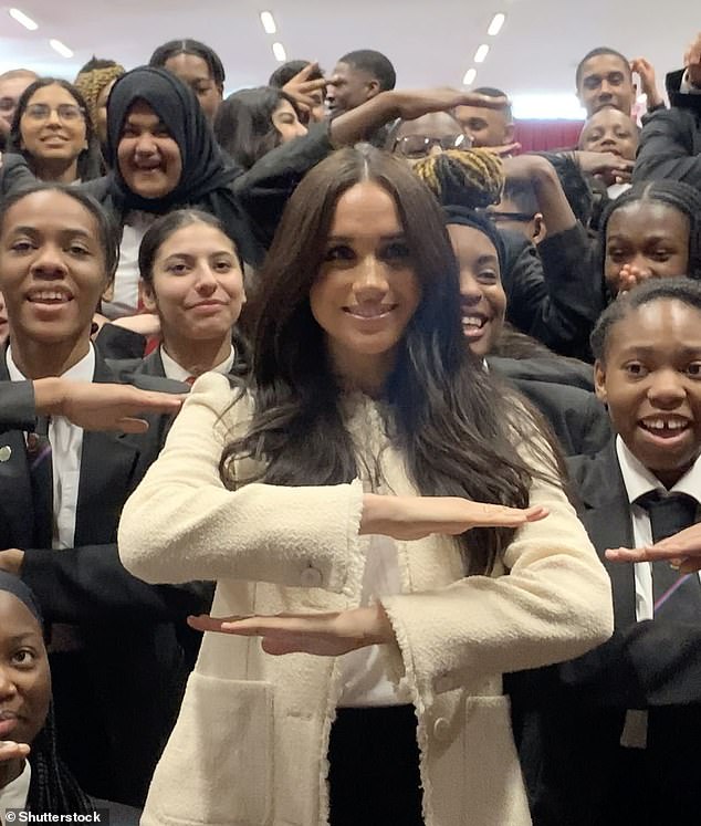 Meghan with schoolchildren doing the 'each for equal' sign during a visit to Robert Clack School in Essex