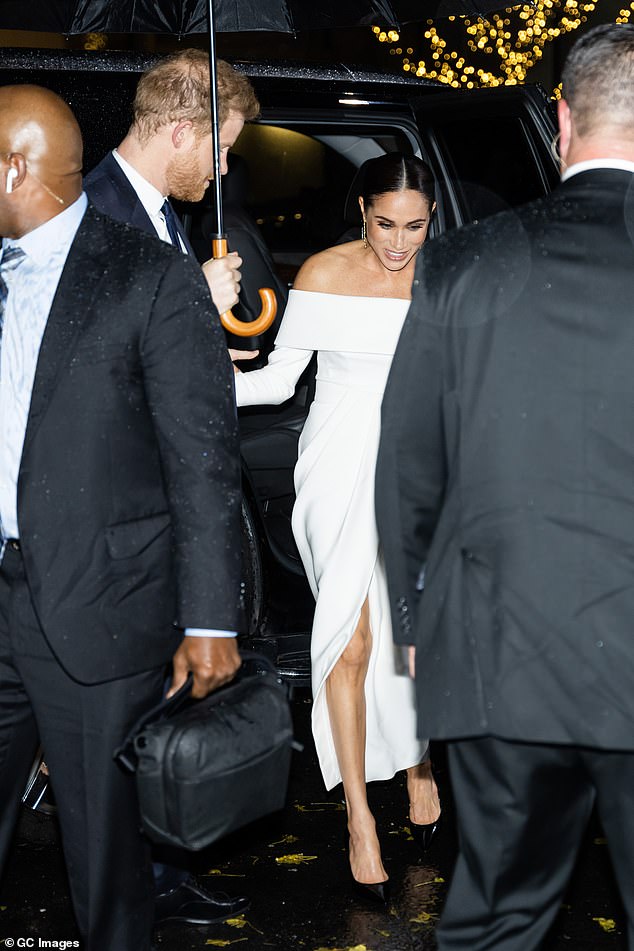 Harry holds an umbrella for Meghan as she steps out of a car in New York in December 2022. The pair are surrounded by security guards