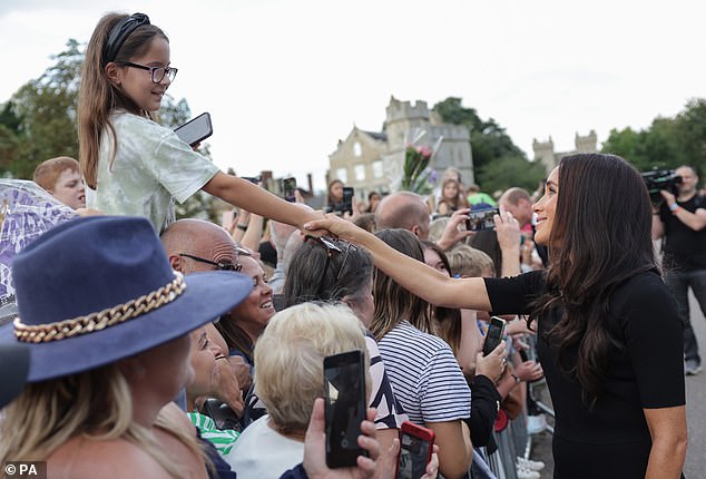 The Duchess of Sussex shakes the hand of a little girl perched on her father's shoulders