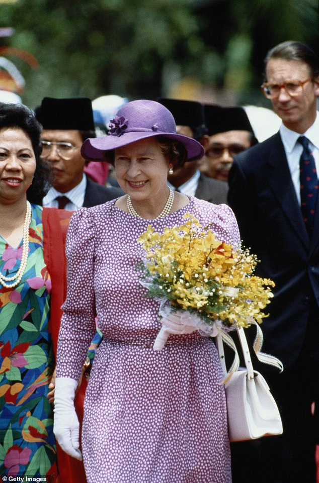 The late Queen, carrying a small bouquet of flowers, and her private secretary, Sir Robert Fellowes (to the right of the image) during a state visit to Malaysia in October 1989