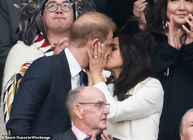 The Duchess wore a $2,590 creme wool trench coat from one of her favourite brands, Sentaler, over a simple olive green knit dress as she packed on the PDA from the stands