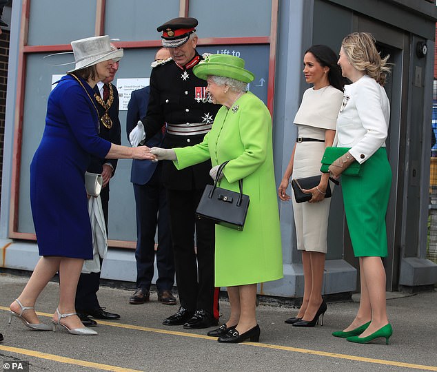 In this photo, Meghan stays behind the Queen while she shakes a woman's hand