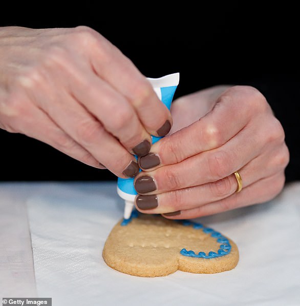 Sophie decorates a biscuit with blue icing as she wears chocolate brown nail polish